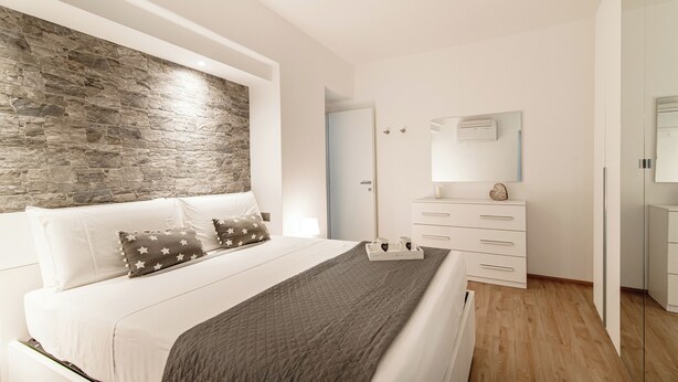 Una camera da letto moderna con una parete decorata in pietra, un letto con cuscini a motivi stellati, un comodino con una lampada e un comò con cassetti.