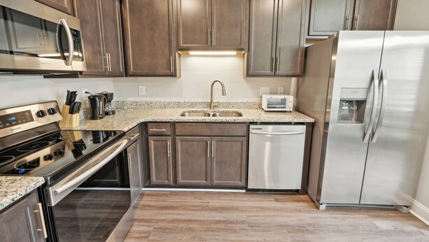Una cocina moderna con armarios de madera oscura, electrodomésticos de acero inoxidable, encimera de granito y lavavajillas.