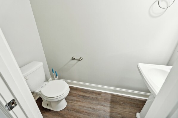 Un baño pequeño y limpio con inodoro y lavamanos blancos, y piso de madera.