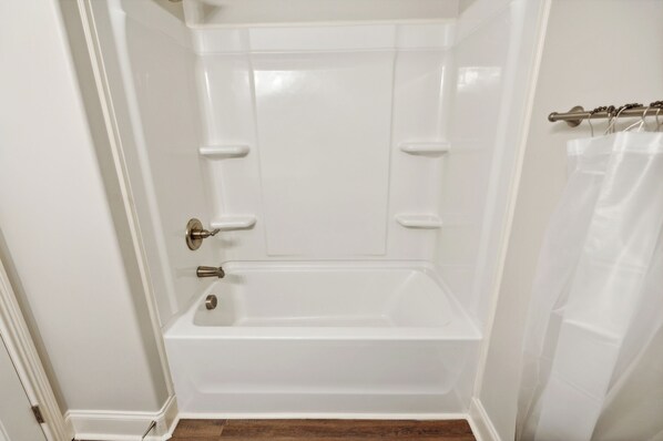 A white bathroom with a bathtub, a shower curtain, and a door with a handle.