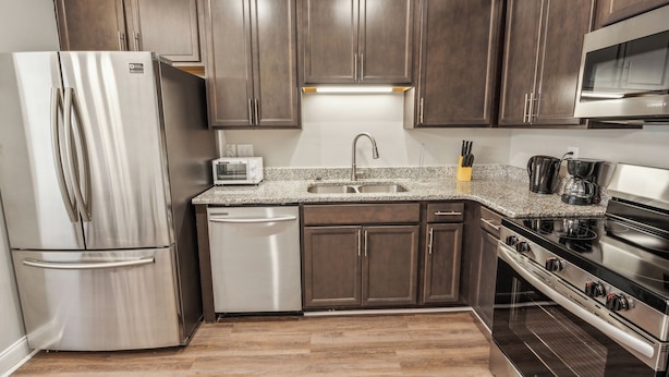 A modern kitchen with stainless steel appliances, dark wood cabinets, and a granite countertop.