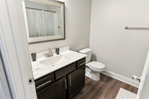 Bathroom features a sink, toilet, and mirror, with a towel rack and dark wood flooring.