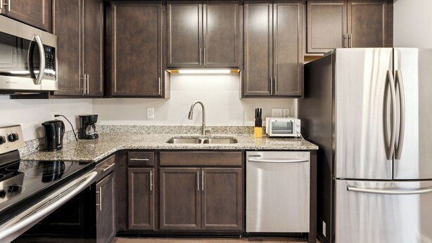 A modern kitchen with dark wood cabinets, stainless steel appliances, and a granite countertop.