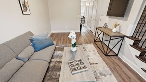 A living room with a grey sofa, a coffee table with a 'XOXO' design, and a wooden console table with a vase and picture frame.