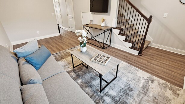 A living room with a gray sofa, a coffee table with a vase of flowers, and a staircase with a wooden railing.