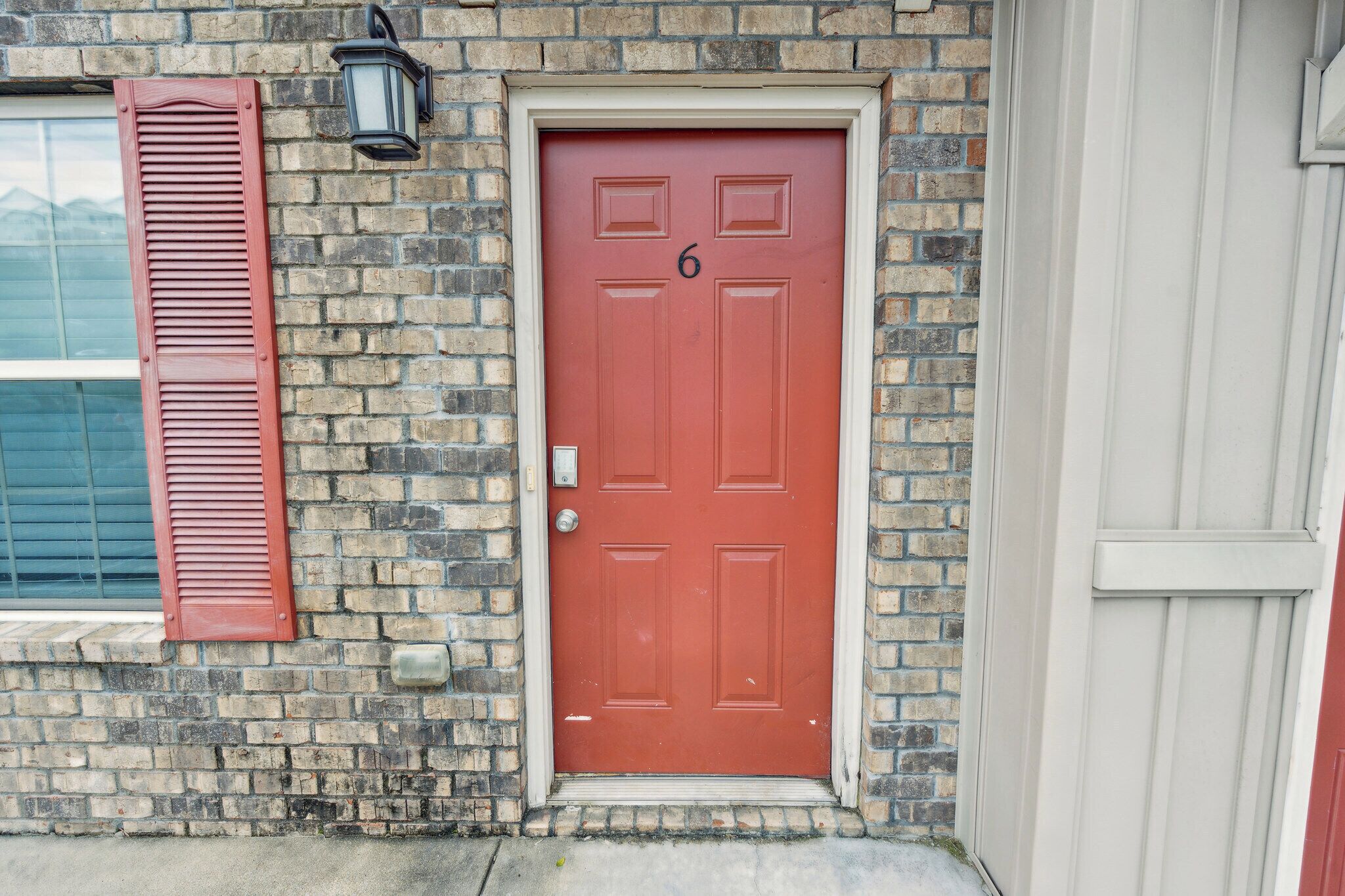 A red door with the number 6, a brick wall, and a window with shutters.
