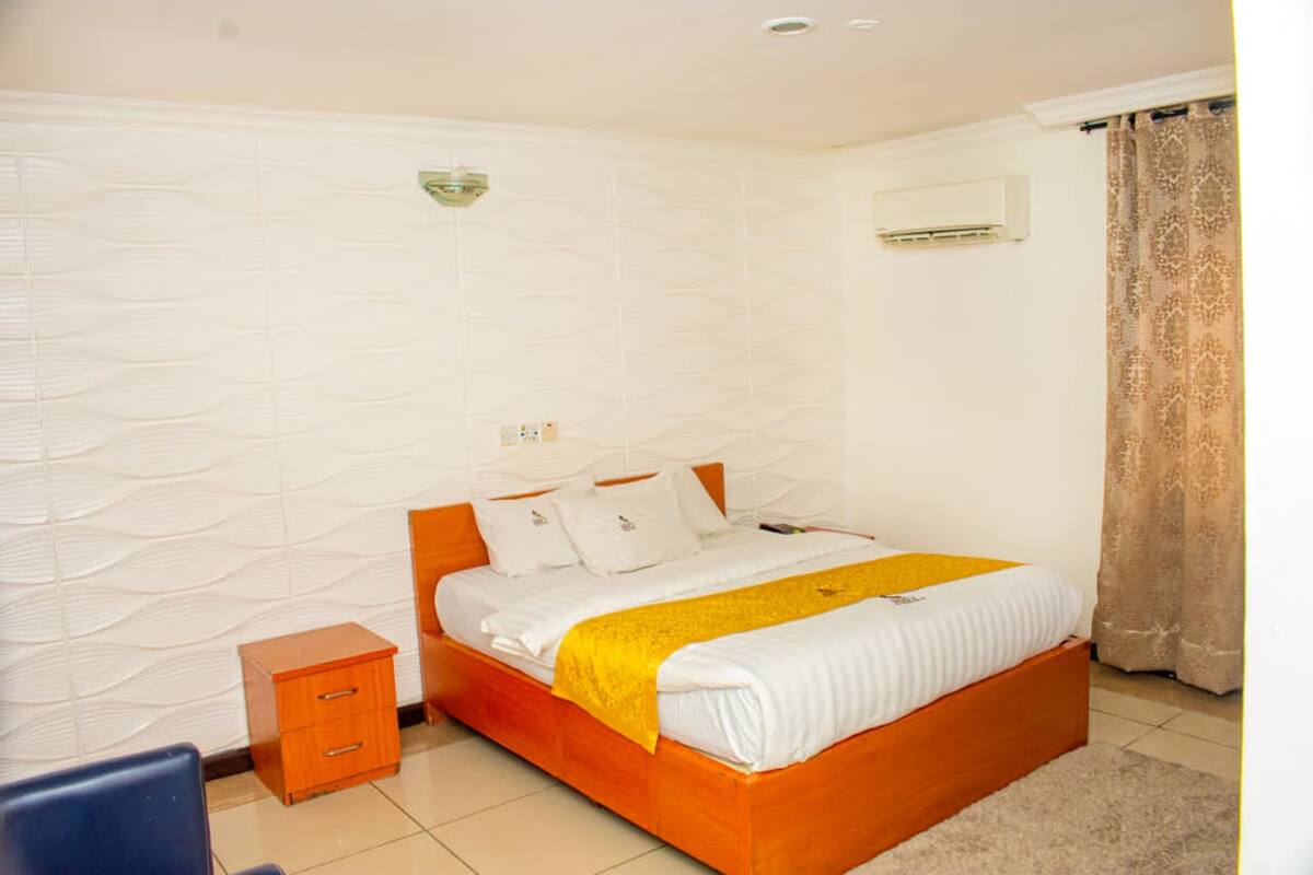 A bedroom with a bed, a nightstand, a wall-mounted air conditioner, and a patterned curtain.
