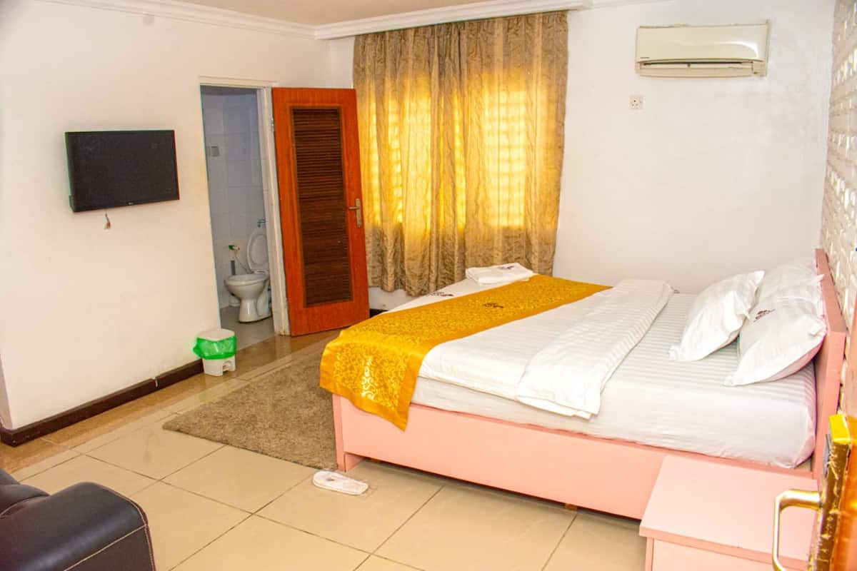 A hotel room with a bed, a television, a bathroom with a toilet, and a door.