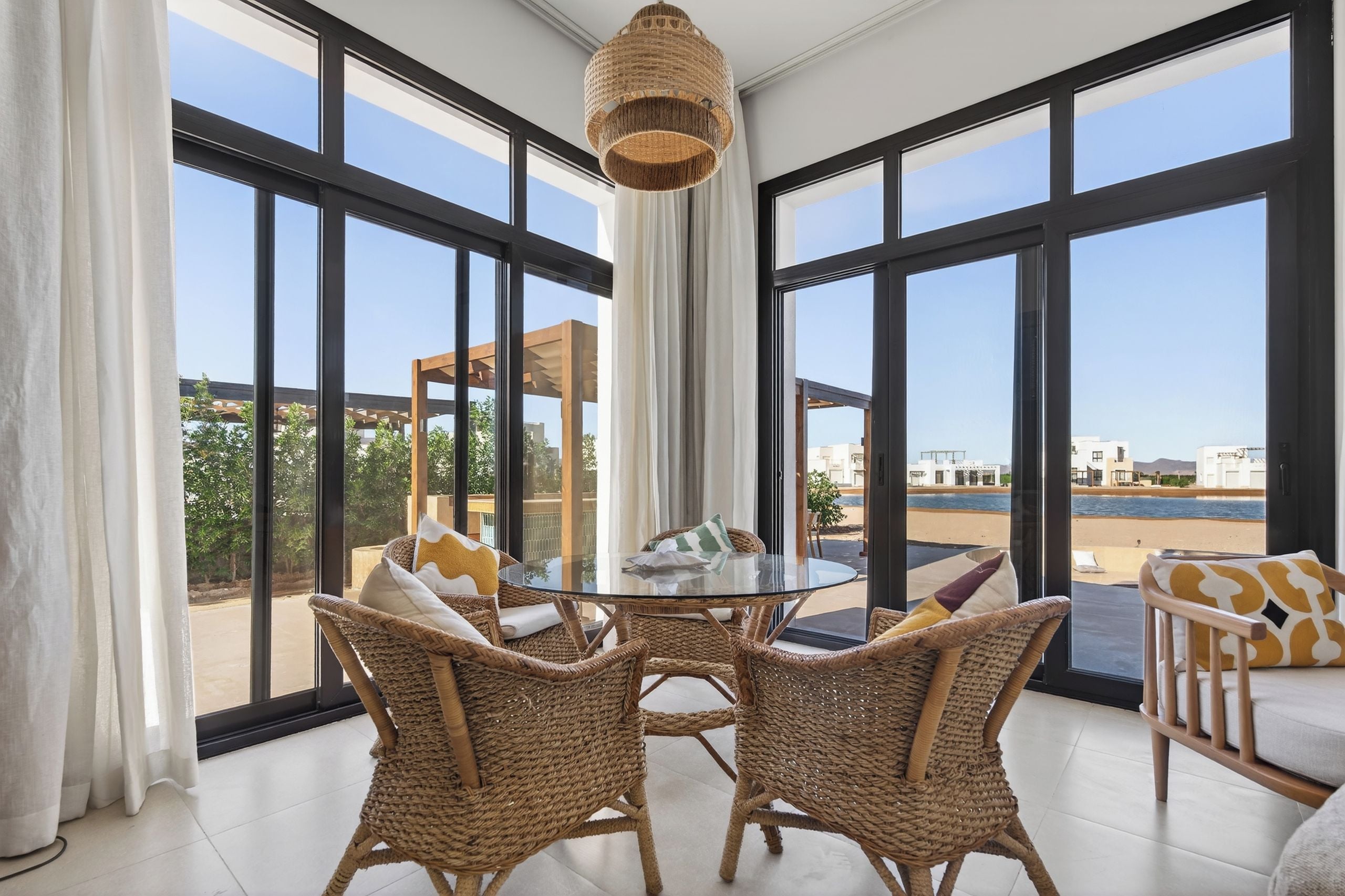 A room with large windows, wicker furniture, and a view of the beach.