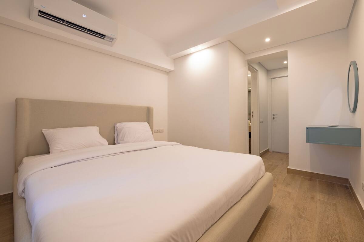 Een slaapkamer met een groot bed, een nachtkastje, een spiegel en een airconditioning.