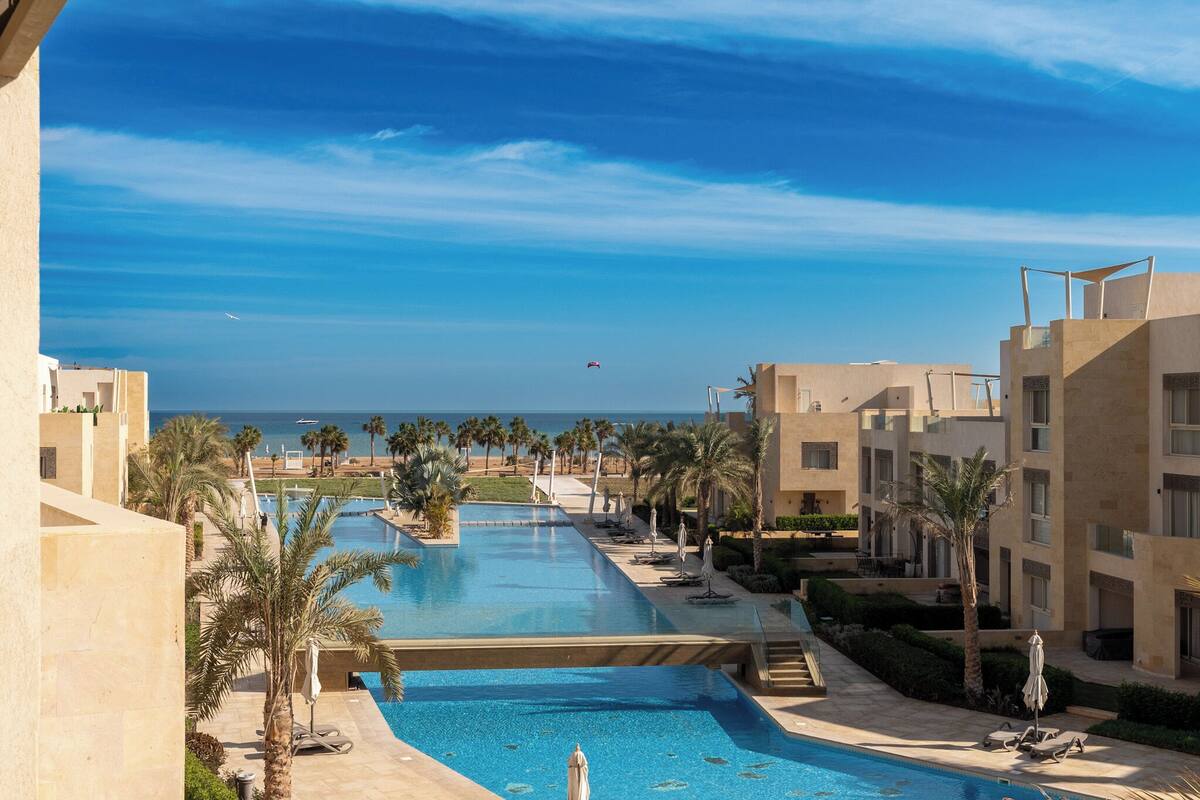 Een resort met een groot zwembad, palmbomen en uitzicht op de oceaan.