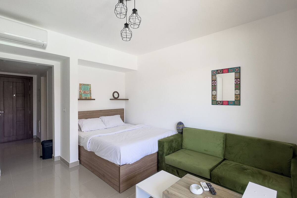 Een moderne hotelkamer met een houten bed, een groene bank, een kleine witte tafel en een decoratieve spiegel.