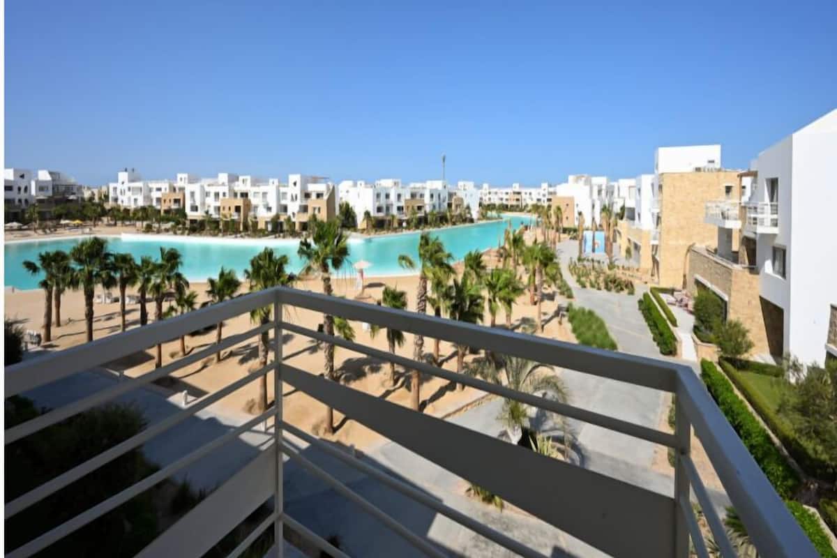 Een resort met een zwembad, palmbomen en een helderblauwe lucht.