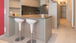 Una cocina moderna con una isla central, dos taburetes blancos de bar y una campana extractora de acero inoxidable.