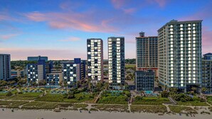 Ein moderner Hotelkomplex mit mehreren Hochhäusern, einem Strandbereich mit Sonnenschirmen und blauem Himmel.