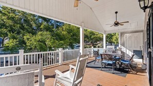 A covered porch with a wooden deck, white railings, and a table with chairs.