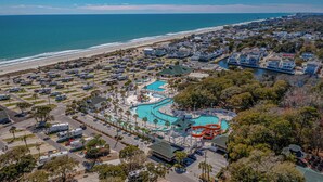 An aerial view of a coastal resort with a large swimming pool, RV parking, and beachfront access.