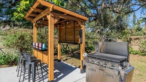 An outdoor barbecue area with a wooden pergola, a stainless steel grill, and a table with chairs. - Heated Salt Water Pool & Fire Pit Retreat in Sarasota (Sarasota)