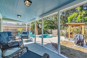 A covered patio area with outdoor furniture, a pool, and a barbecue setup.