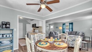 A dining area with a round table, chairs, and a ceiling fan. There is a kitchen in the background with cabinets and a microwave. - Heated Salt Water Pool & Fire Pit Retreat in Sarasota (Sarasota)