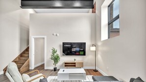 Un salon moderne doté d’un téléviseur à écran plat, d’un escalier en bois et d’un design minimaliste.