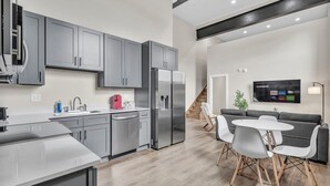 Une cuisine moderne avec des meubles gris, un réfrigérateur en acier inoxydable et un coin repas comprenant une table blanche et des chaises grises.