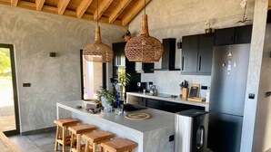 Una cocina moderna con una isla central, taburetes de bar, lámparas colgantes de mimbre y un refrigerador empotrado.