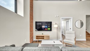 Ein modernes Wohnzimmer mit einem großen Flachbildfernseher an der Wand, einem weißen Couchtisch, grauen Sofas und einem Holz-TV-Möbel.
