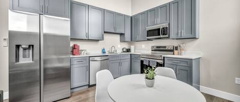 A modern kitchen with grey cabinets, stainless steel appliances, and a round dining table with chairs.