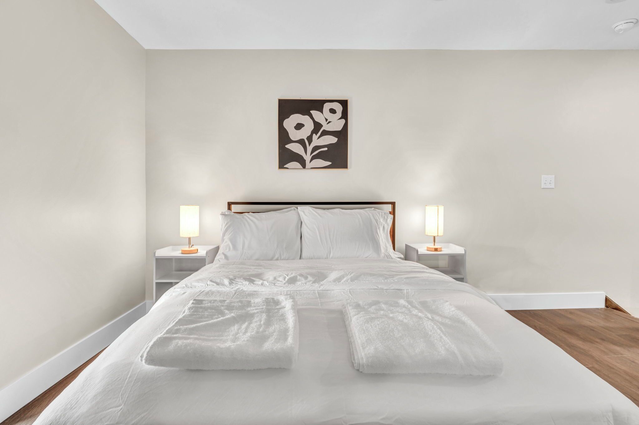 A neatly made bed with white linens and two bedside lamps.