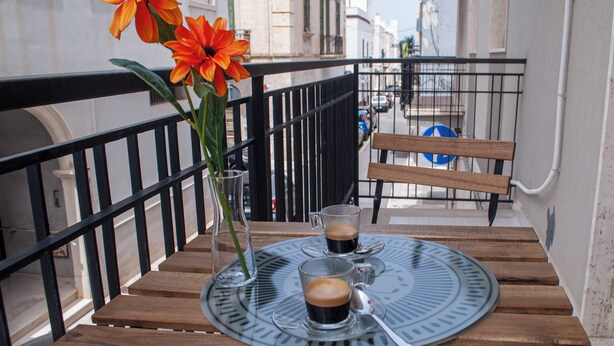 A wooden table with two glasses of coffee and a vase with flowers on a balcony.