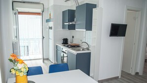 A compact kitchen with a dining area, a TV mounted on the wall, and a window with curtains.