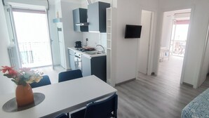 A modern kitchen with a gas stove, sink, and cabinets, a dining area with a table and chairs, and a living space with a sofa and a TV.