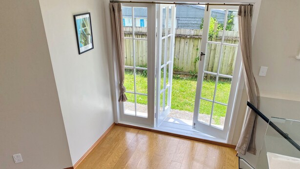 Ein Zimmer mit Holzboden, einer Schiebetür zu einem Garten und einem gerahmten Bild an der Wand.