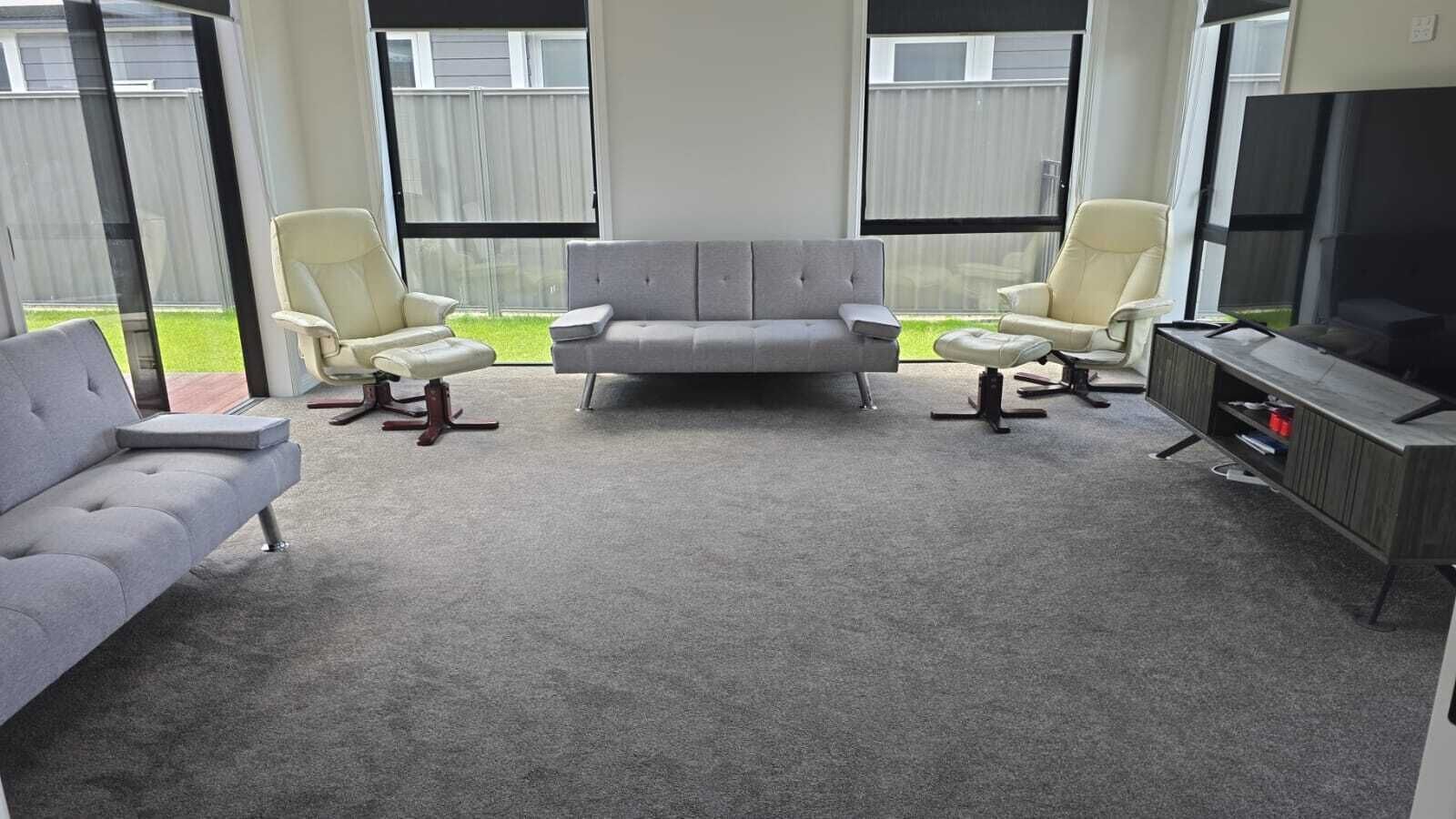 A living room with a grey sofa, two armchairs, a coffee table, and a TV stand.