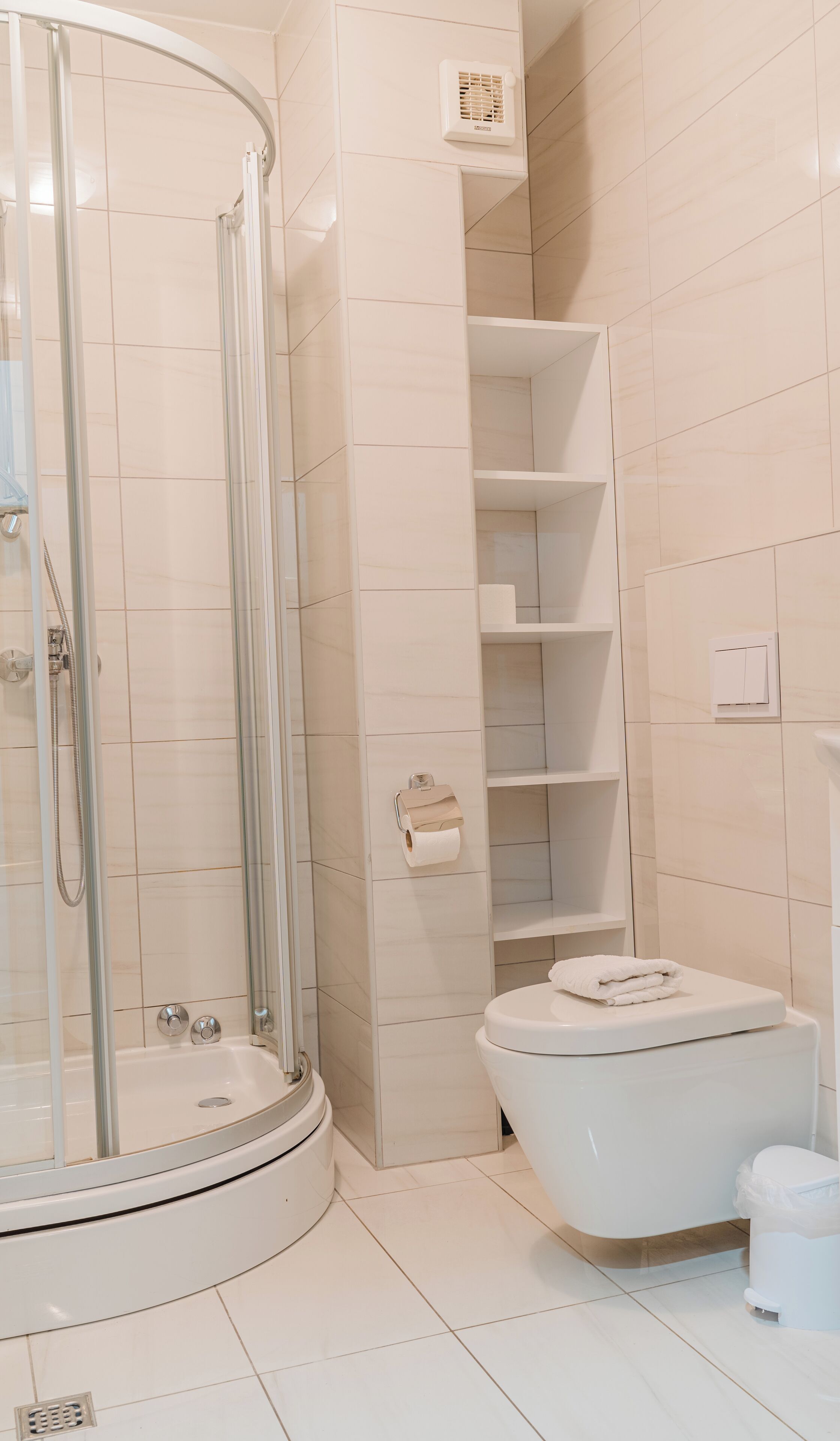 Une salle de bain moderne dotée d’une douche à parois de verre, de toilettes et d’étagères intégrées.