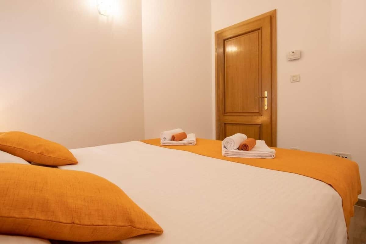 A hotel room with a bed, two orange pillows, and a wooden door.