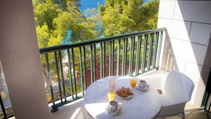 Ein Balkon mit Frühstückstisch, gedeckt mit Croissants, Kaffee und Orangensaft, mit Blick auf eine schöne Landschaft aus Meer und Bäumen.