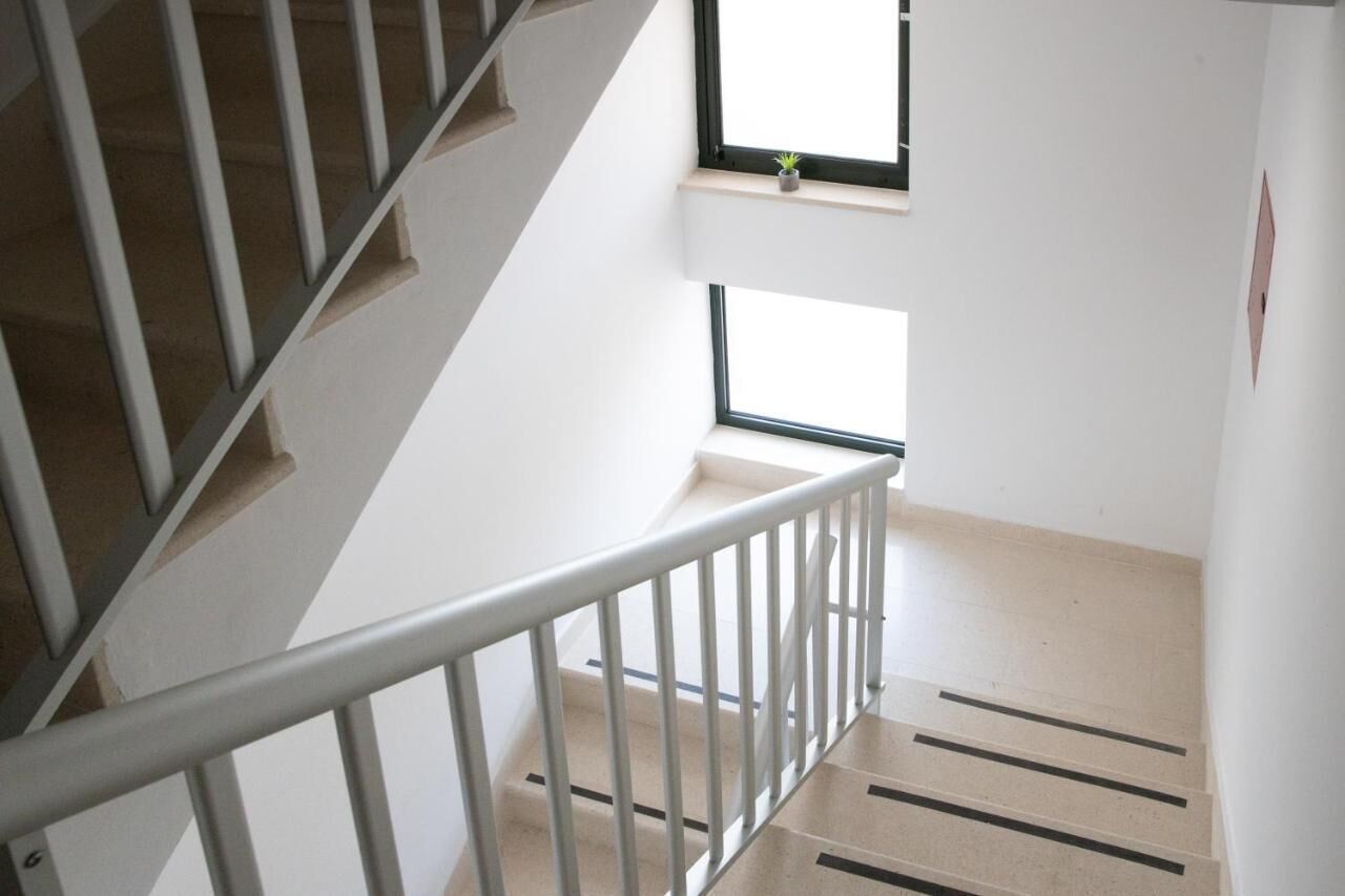 Un escalier avec une rampe en métal, une petite fenêtre ornée d’une plante et un mur blanc.