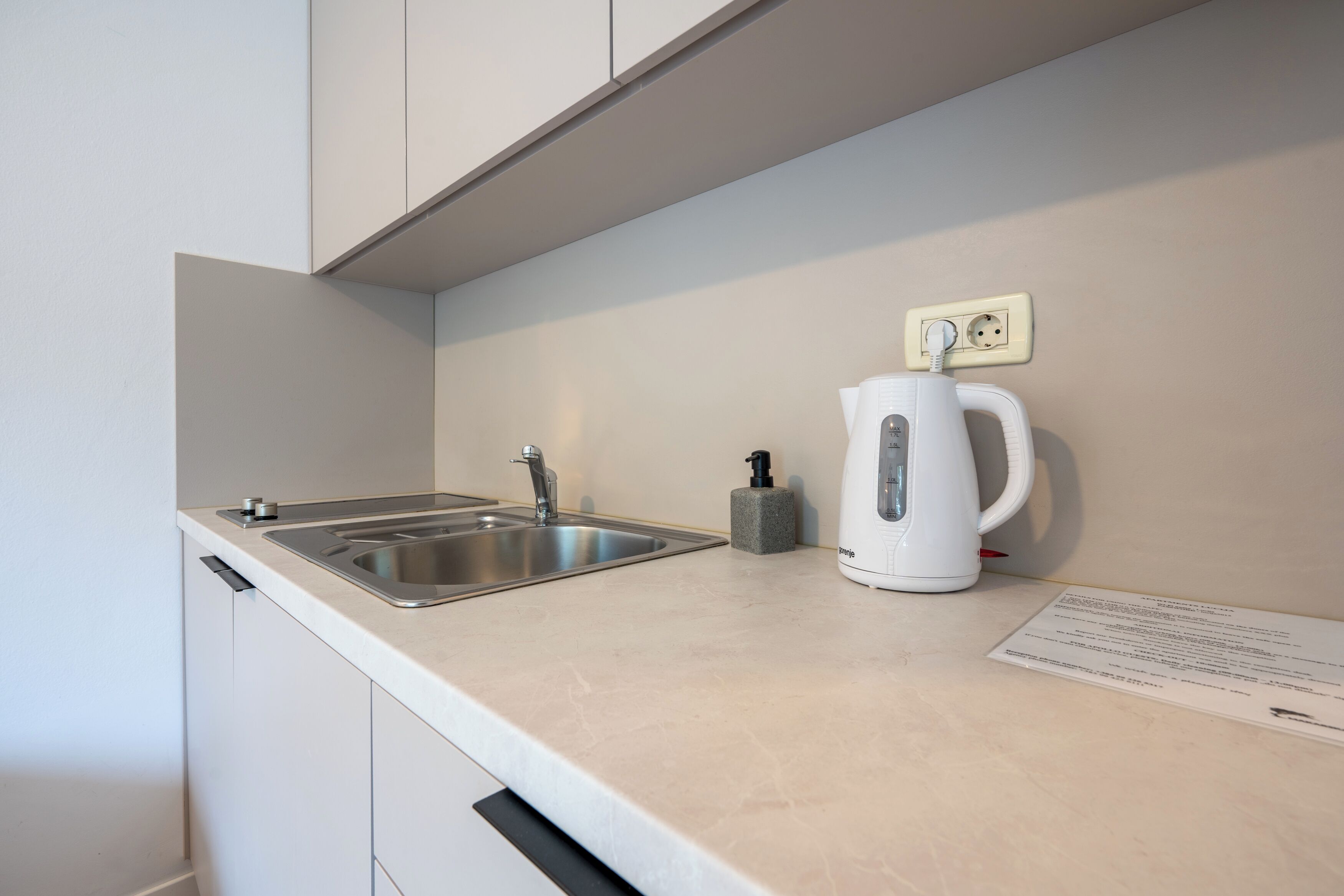Una cocina moderna con un lavamanos doble, un hervidor y un dispensador de jabón.