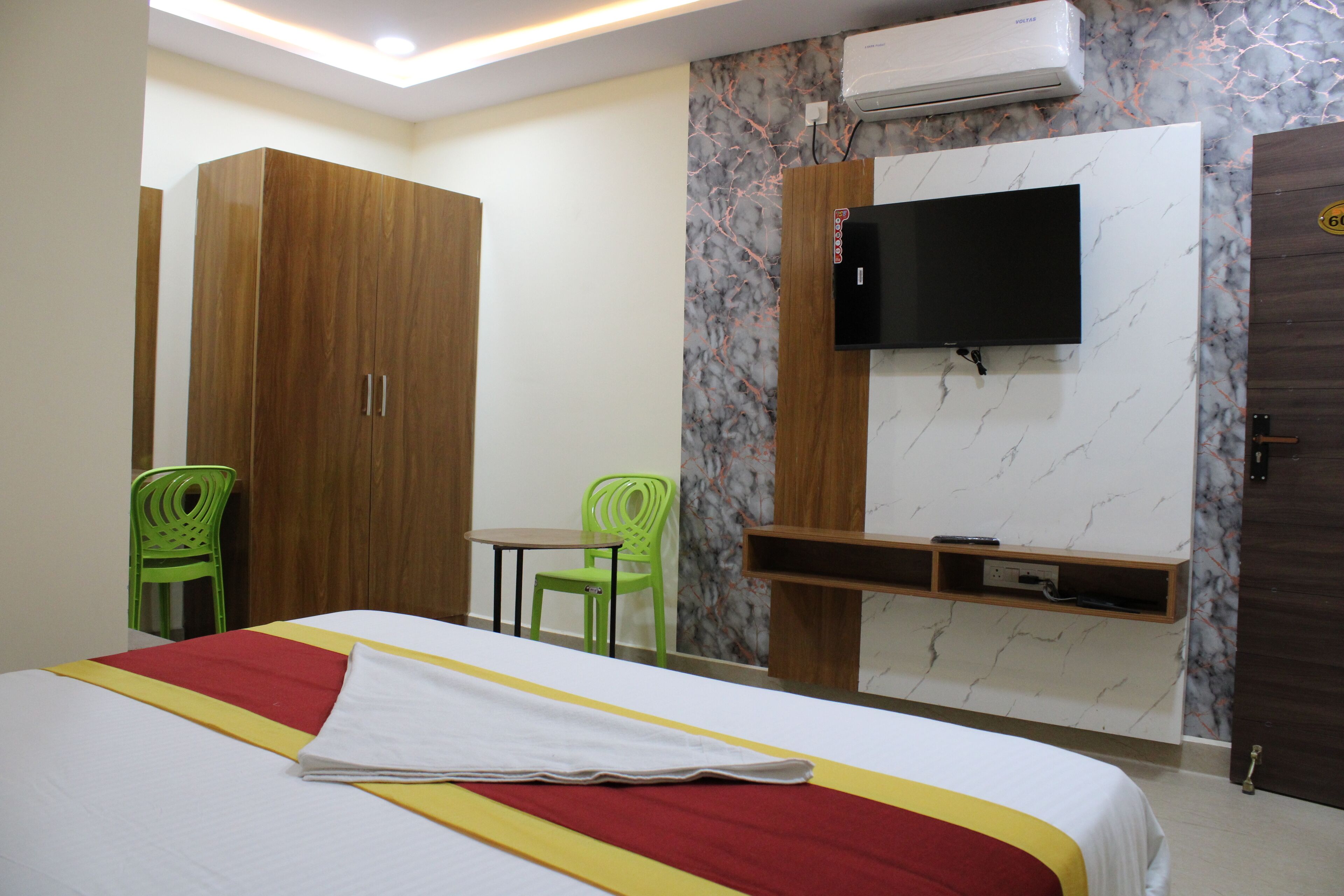 Una habitación de hotel con una cama, un televisor montado en la pared, un escritorio y dos sillas.