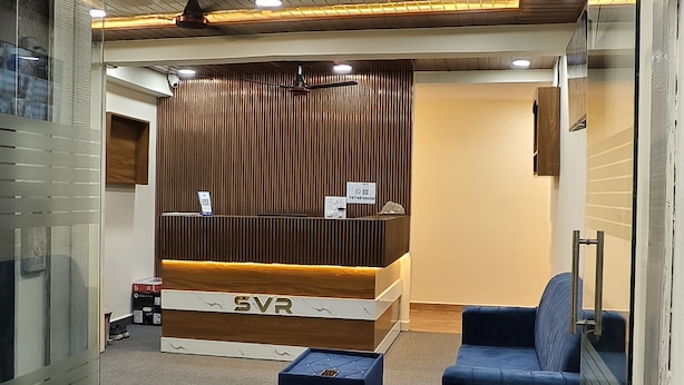 Een hotellobby met een receptiebalie, een blauwe bank en een bord waarop staat: Hotel SVR Luxury Rooms.
