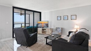 Una sala de estar moderna con un televisor grande, dos sofás, una mesa de centro y vista al agua.