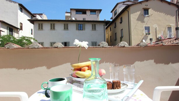 A table with a green mug, a clear bottle, a plate with fruit, and a white flower. - Marsili Suite (Florence)