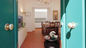 A dining area with a table set for two, a chandelier, and a kitchen in the background. - Marsili Suite (Florence)