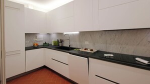 A modern kitchen with white cabinets, a black countertop, and a marble backsplash. - Marsili Suite (Florence)