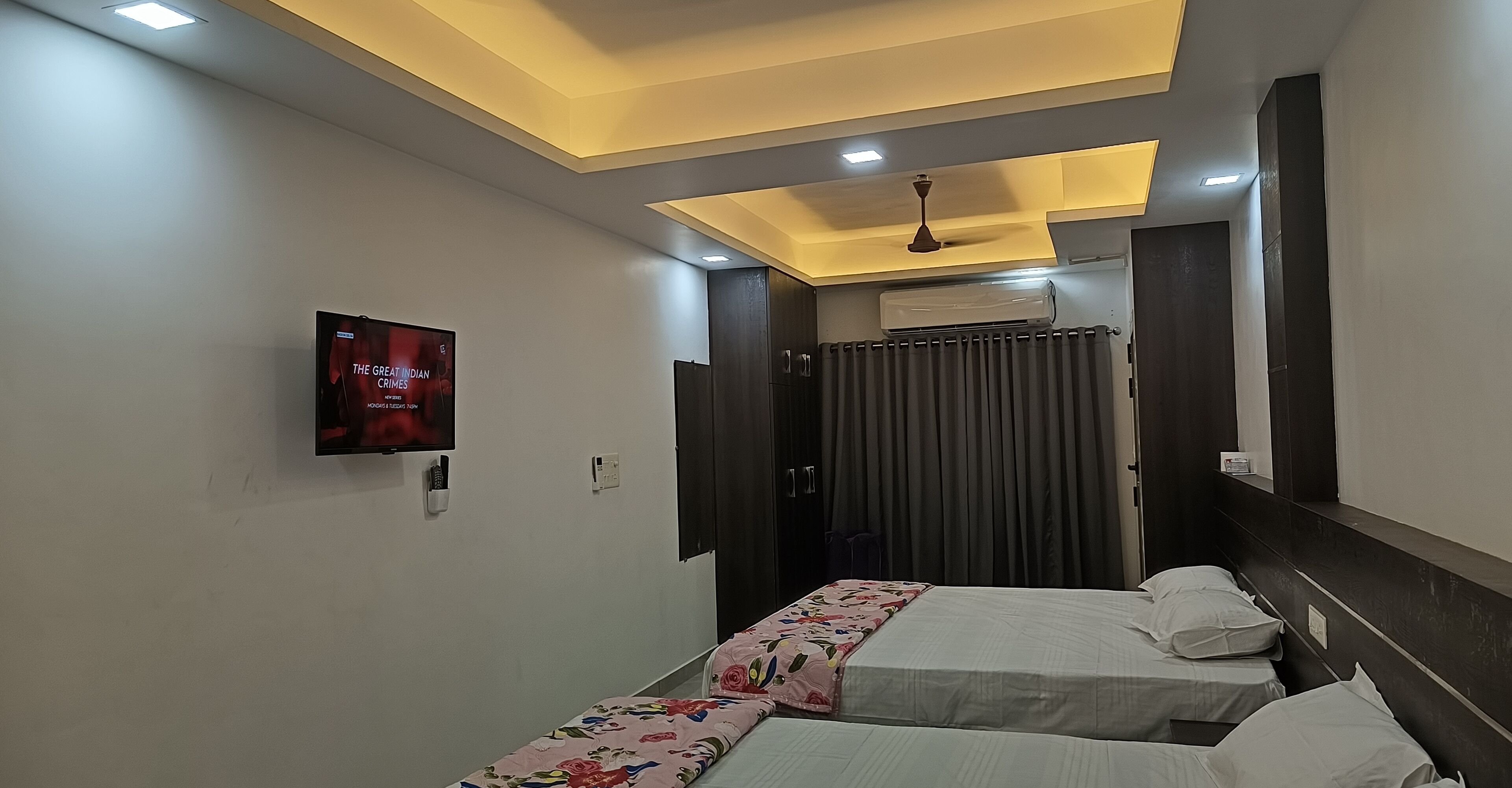 Une chambre d’hôtel avec deux lits, une télévision, un ventilateur de plafond et une fenêtre avec des rideaux.