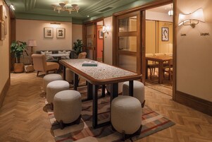 Ein Hotelzimmer mit einem großen Holztisch, vier Poufs, einer Couch und einem Esstisch mit Stühlen.