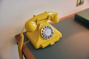 A yellow rotary dial telephone on a wooden table.