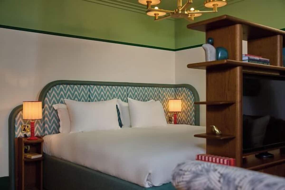 A hotel room with a bed, nightstands, lamps, a television, and a bookshelf.